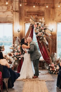 a bride and groom kissing in front of an arch decorated with floral arrangements at their wedding