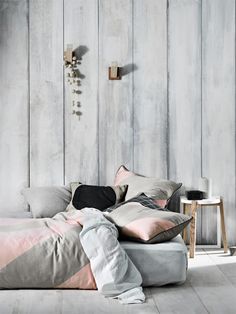 a bed with pink and grey pillows on top of it next to a wooden wall