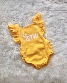 a yellow onesuit with the word mom on it sitting on a fluffy white rug