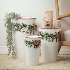 three white christmas planters with holly and berries painted on them, sitting next to a chair