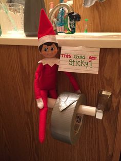 an elf with a sign hanging from the wall next to a roll of toilet paper