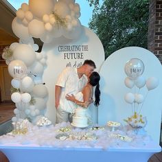 a man and woman kissing in front of a table covered with white balloons, cake and confetti