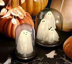 two glass domes with white ghost decorations on them and pumpkins in the back ground