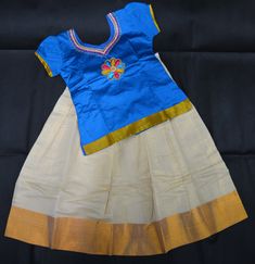 This beautiful girls' outfit features a vibrant blue silk blouse adorned with intricate Aari work on the neckline, showcasing detailed floral embroidery. The cream silk skirt is highlighted with a golden border, creating a striking contrast. Brand - SaaiB Features: Blouse: Blue silk with Aari embroidery Skirt: Cream tissue silk with a golden border Closure: Hook and Knot at the back for easy wear Design: Perfect for festive occasions This elegant and traditional ensemble is a perfect addition to Traditional Blue Sets With Gold Embroidery, Navratri Gold Sets With Embroidered Border, Gold Cotton Anarkali Set With Zari Work, Gold Cotton Anarkali Set For Festive Occasions, Blue Art Silk Sets With Embroidered Border, Blue Traditional Wear With Gold Embroidery For Diwali, Traditional Blue Skirt Set For Festivals, Traditional Blue Festive Skirt Set, Blue Cotton Lehenga With Pallu