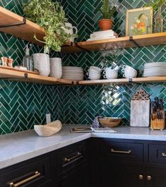 a kitchen with green tiled walls and shelves filled with dishes, cups, bowls and vases