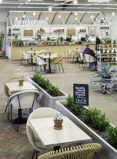 the inside of a coffee shop with tables, chairs and potted plants on display