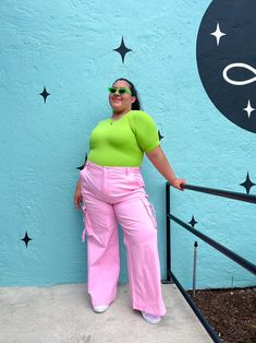 a woman in pink pants and green shirt leaning against a blue wall with stars on it