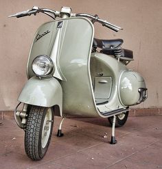 an old scooter is parked on the side of the street near a wall