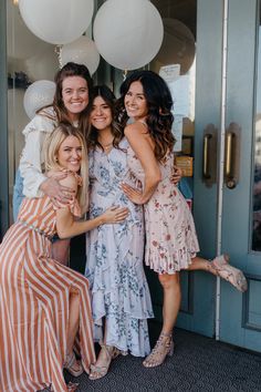 four women are posing for the camera in front of a door with white balloons behind them