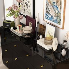 a black dresser topped with lots of clutter next to paintings and pictures on the wall