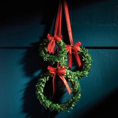 a green wreath with red bows hanging on a blue wooden wall next to a pair of scissors