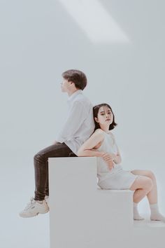 a man and woman sitting on top of a white box with their arms around each other