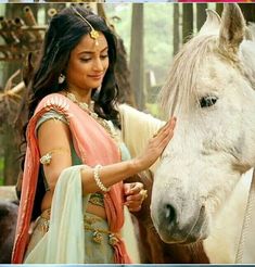 a woman standing next to a white horse wearing a sari and holding the reigns