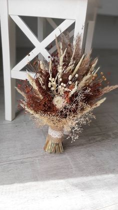 a bouquet of dried flowers sitting on top of a white table next to a chair