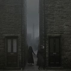 two women are walking through an alley way in the dark with their hands on each other's backs