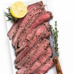 sliced steak on a white plate with lemon wedges and parsley next to it