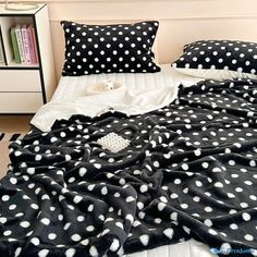 a bed with black and white polka dot comforter on it, next to a bookcase