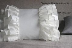 a white pillow with ruffles on it sitting on top of a gray bed