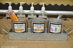 three cups with pencils and markers in them sitting on a metal tray next to some bottles