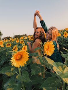 two beautiful young women standing next to each other in a field of sunflowers