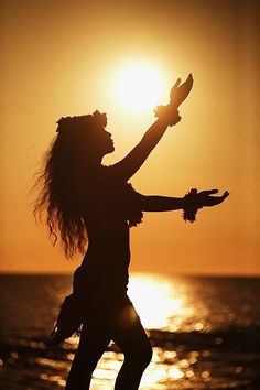 a woman standing on top of a beach next to the ocean holding her arms up