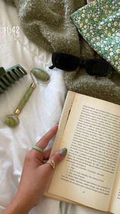 a person laying in bed reading a book with sunglasses on top of it and other items nearby