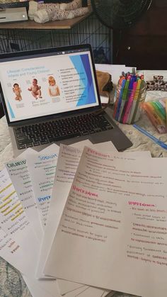 an open laptop computer sitting on top of a pile of papers next to a stack of crayons