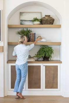 a woman standing in front of a bookshelf with plants on top of it