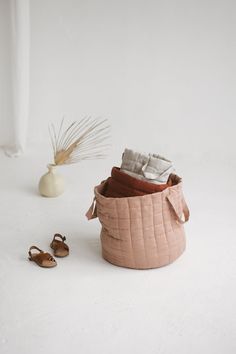 a pair of baby shoes sitting next to a basket with cloths in it and a vase on the floor