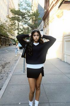 a woman is standing on the sidewalk with her hands behind her head and looking at the camera