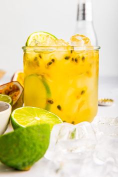 a glass filled with lemonade and limes next to some ice cubes on a table