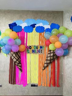 an ice cream cone with balloons and streamers hanging from it's sides in front of a wall