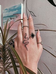 a woman's hand with a snake tattoo on it and a plant in the background