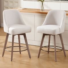 two white bar stools sitting next to each other on a wooden floor in front of a counter