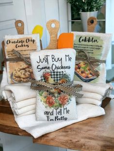 kitchen towels with sayings on them sitting on a wooden table next to utensils