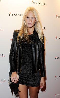 a woman in a short black dress and leather jacket posing for the camera at an event