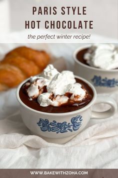 two cups of hot chocolate with whipped cream on top and croissants in the background