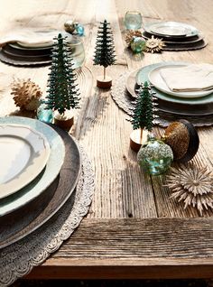 a wooden table topped with plates and place settings covered in christmas tree decorations on top of it