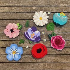 several felt flowers on a wooden surface with leaves and flowers in the middle one flower is blue, pink, purple, and white