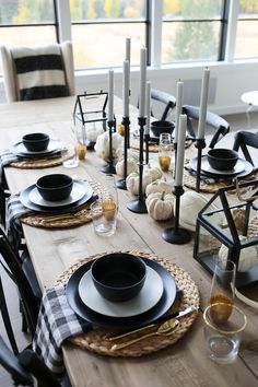 a dining room table set with black and white place settings, pumpkins on the tables