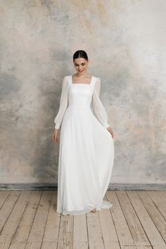 a woman wearing a white dress standing in front of a wall