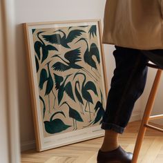 a person sitting on a stool next to a framed art piece with birds in it