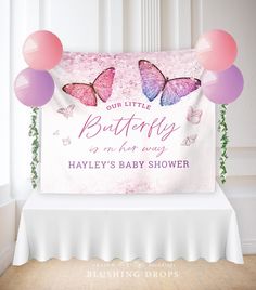 a baby shower sign with pink and purple butterflies on it's back, in front of a white backdrop