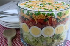 a layered salad with hard boiled eggs, bacon, peas and cheese in a glass bowl