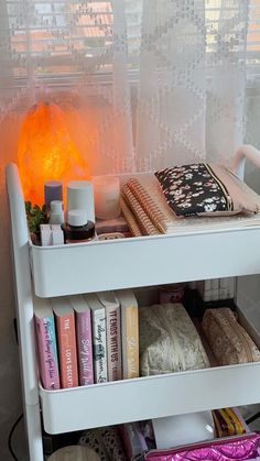 a shelf filled with books and other items next to a window covered in sheer curtains