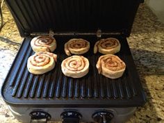 six cinnamon rolls are cooking on an outdoor grill