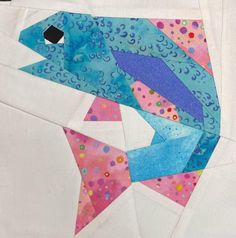 a fish made out of paper on top of a piece of white fabric with blue and pink colors