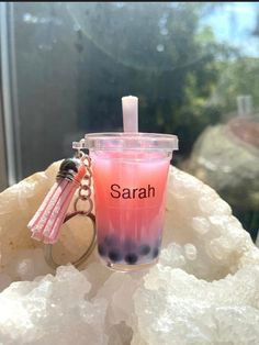 a pink drink sitting on top of a rock next to a keychain with the word sarah written on it