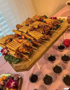 a wooden table topped with waffles and other foods on skewers next to bowls of dipping sauce