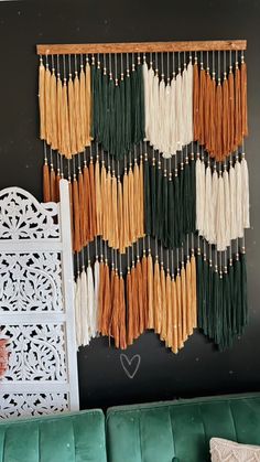 a wall hanging made out of different colored yarns on a black wall next to a green couch